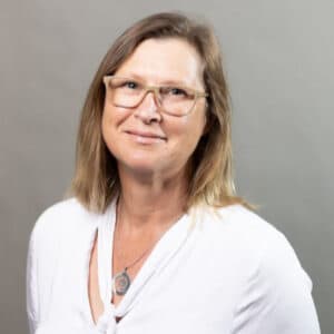 Profile photo of Catherine Chicken standing in front of a grey wall. 