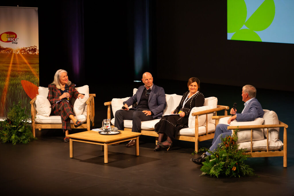 Pannell of 4 people sitting on white lounges, around coffee table on stage, and answering questions for the Australian Rice Growers' Conference