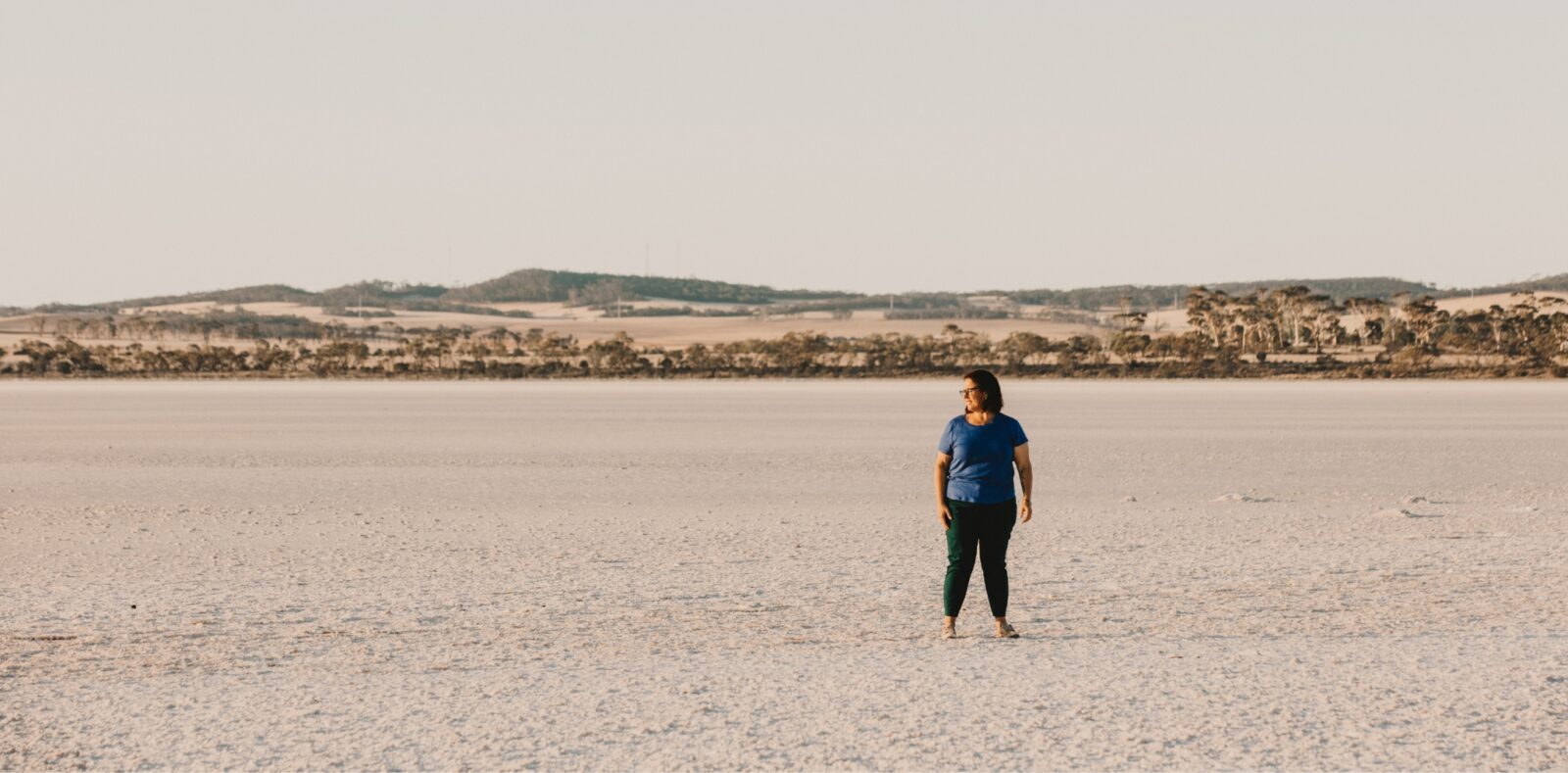 Woman standing on a wide, dry rural landscape with distant hills, symbolising innovation, resilience, and leadership supported by the AgriFutures Rural Women’s Acceleration Grant.