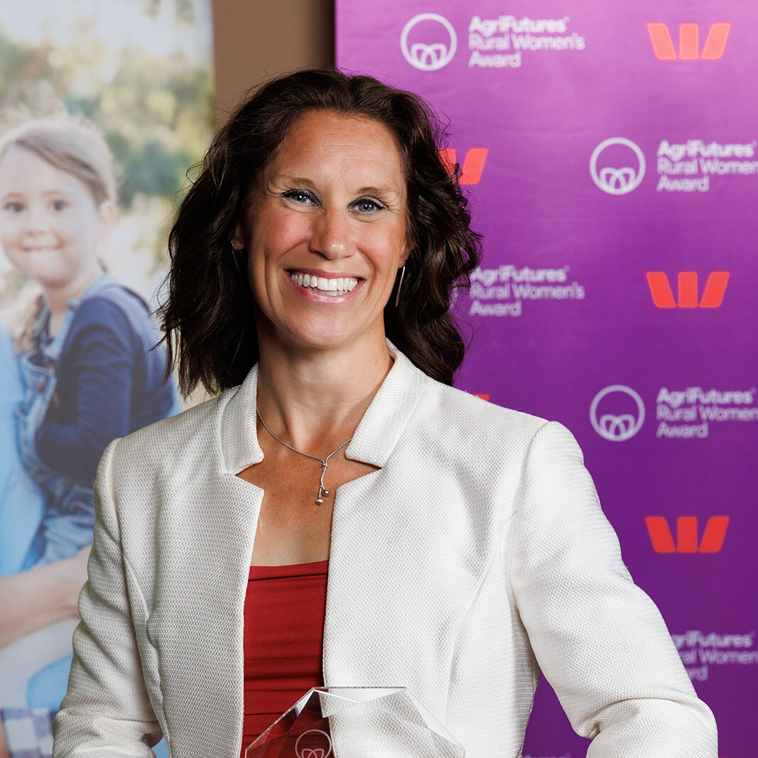 Becky Dickinson stands on stage receiving the 2026 Victorian AgriFutures Rural Women’s Award, holding a glass trophy, with AgriFutures and Westpac logos on a purple banner behind her.