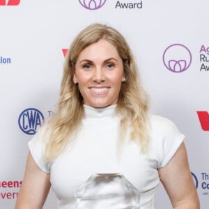 A smiling woman with long blonde hair wearing a white top holds a glass award, recognizing her achievements in agriculture and research, in front of a backdrop with various logos.