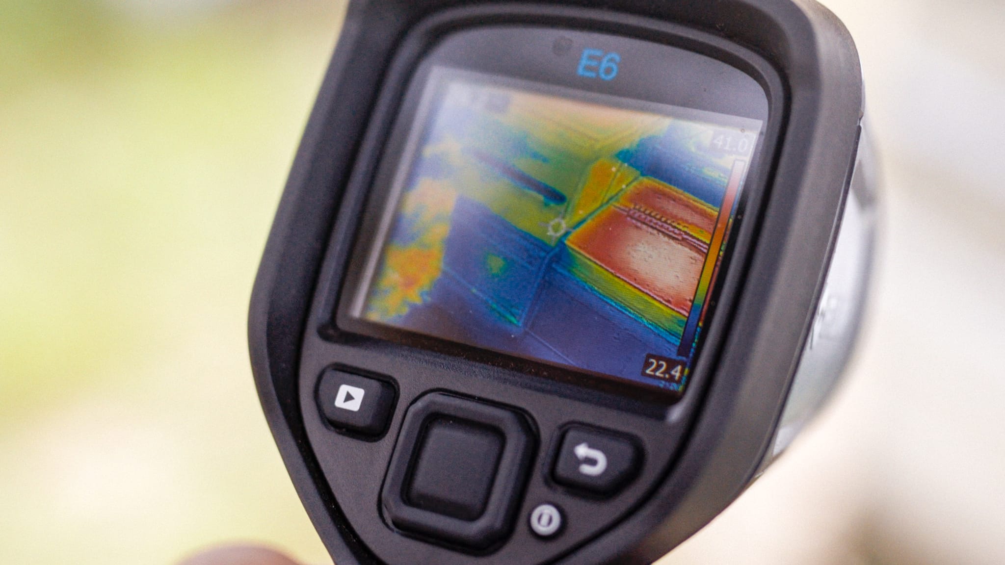 A close-up of a handheld thermal imaging camera displaying a colourful heat map on its screen, with buttons visible beneath the display.