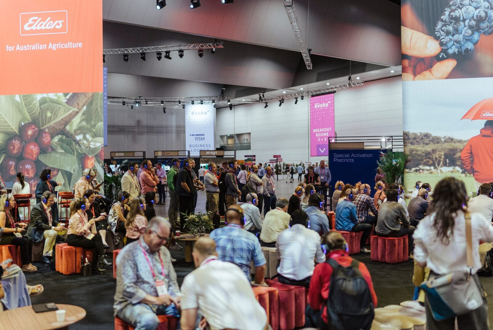 A large group of people sits and stands in a spacious convention hall with banners, including “Elders for Australian Agriculture.” Attendees are engaged in discussion and activities at the event.